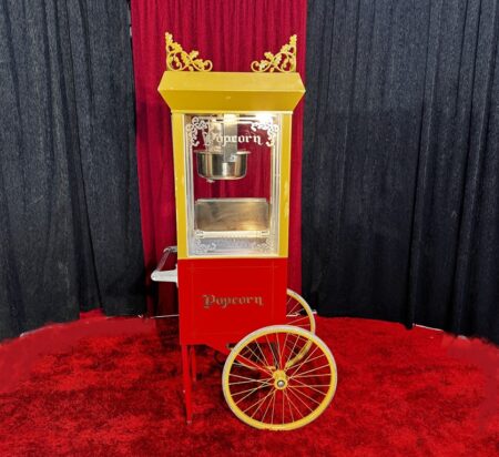 schöne nostalgische popcornmaschine auf rotem edlen teppich vor rot schwarzem vorhang.maschine in gold mit rotem unterwagen auf rädern.