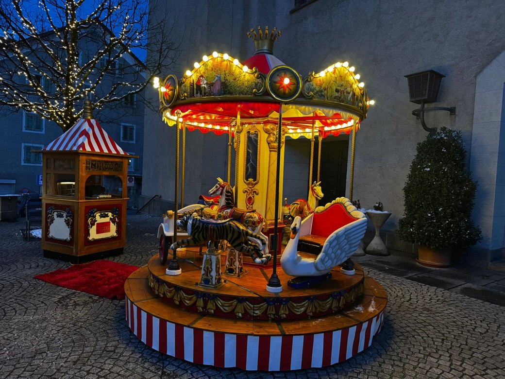 schönes nostalgisches karussell mit lichtern in der abenddämmerung, daneben ein antikes kassenhaus mit licht.