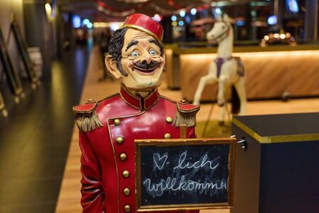 dekofigur mit schnauz und nostalgiekostüm. hält ein schild in der hand mit herzlich willkommen drauf
