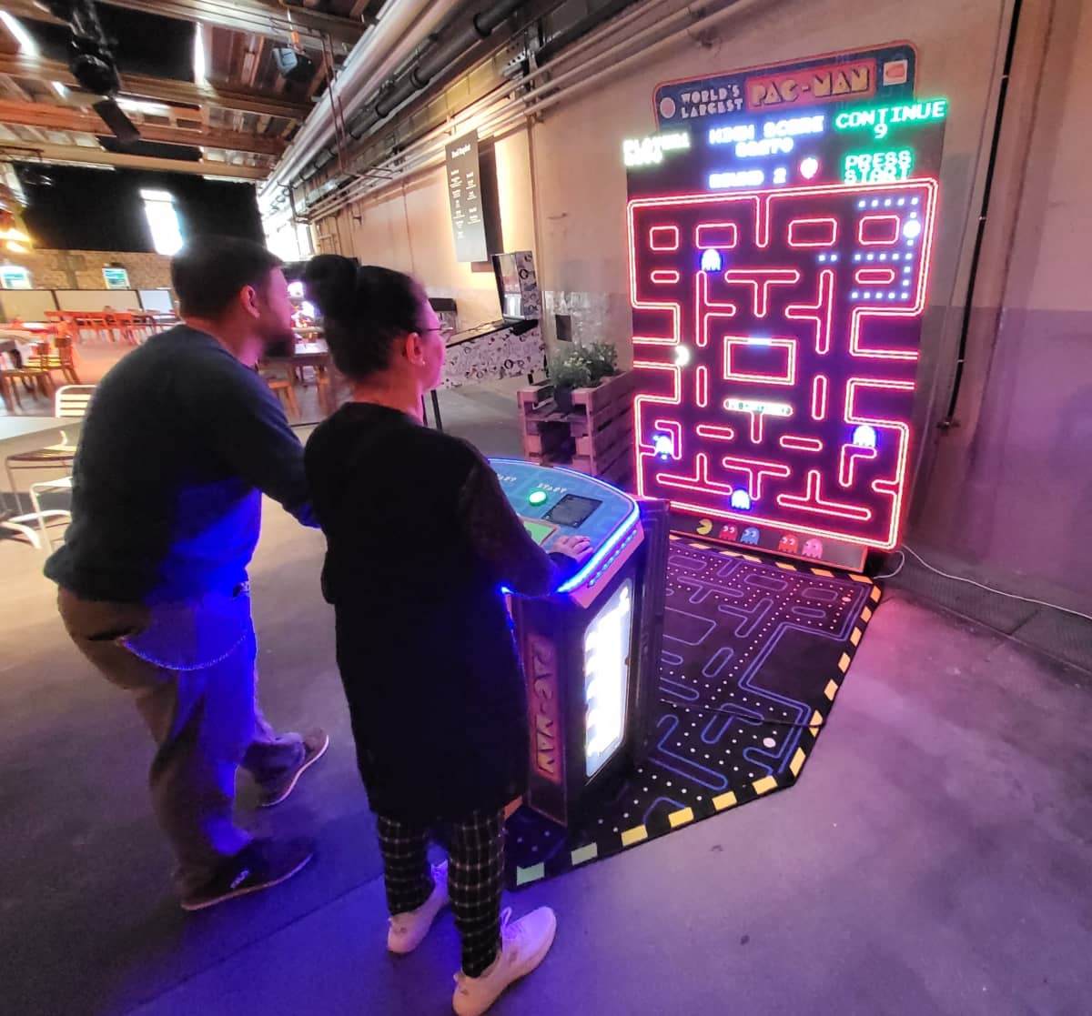 Eine Frau und ein Mann spielen gemeinsam am XXL Pac-Man-Automat.