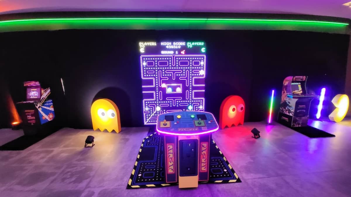 XXL Pac-Man-Automat zwischen zwei klassischen Arcade-Automaten mit angeleuchteten übergroßen Gespenstern und Pacman.